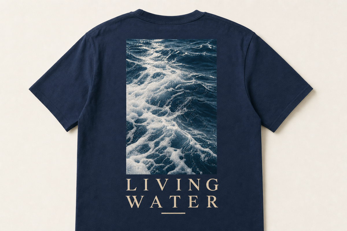 Marineblå t-skjorte sett bakfra med fotomotiv av havbølger over teksten LIVING WATER